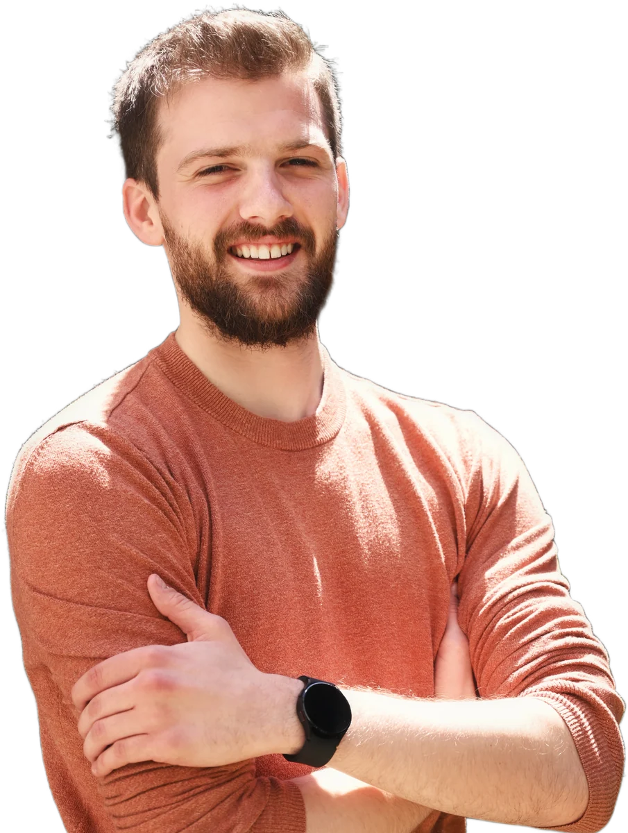 Jamie Harris smiling with his arms folded, wearing an orange jumper